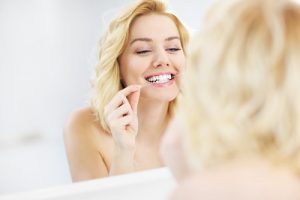 'woman flossing teeth in mirror'